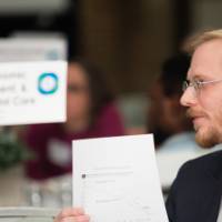 A man references a printed graph while speaking to other attendees as his round table.